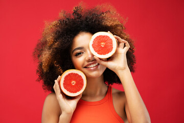 Photo of young cheerful dark skin woman hold grapefruit cover eye look empty space isolated on red...