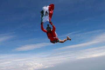 The national flag of Mexico is in the sky. A red skydiver is flying in the sky with Mexican flag.