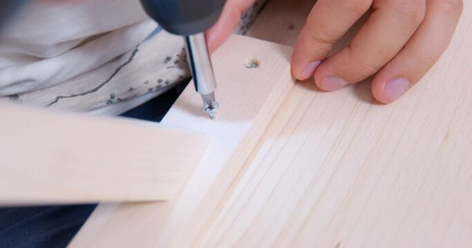 Joiner master drills self-tapping screw on wooden plank board. Master class on making furniture with your own hands. Furniture design handmade. Self-tapping screw smoothly enters wooden board