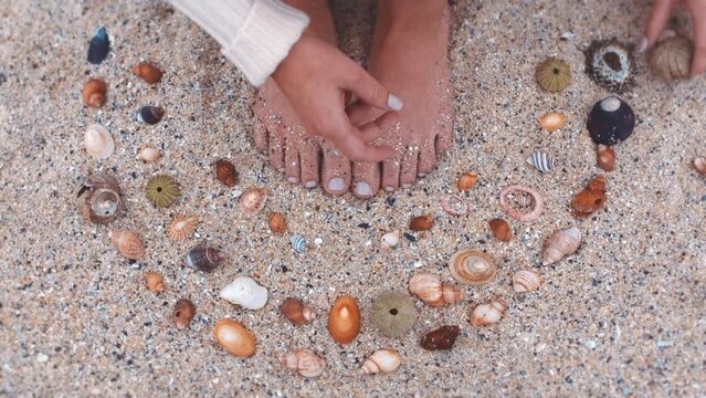 Woman feet, shell and beach sand while sitting barefoot and enjoying tropical holiday travel while collecting souvenirs. Summer, ocean and vacation getaway with circle shape and love for seaside