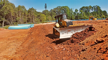bulldozer pushing dirt while grading land with digger in background - obrazy, fototapety, plakaty