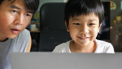 Authentic asian child boy using laptop with father. Kid smile with happy face looking to notebook for studying at home. Education learning, good family relationship, togetherness, home school concept.