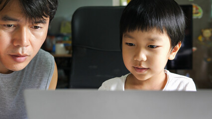 Authentic asian child boy using laptop with father. Kid smile with happy face looking to notebook for studying at home. Education learning, good family relationship, togetherness, home school concept.