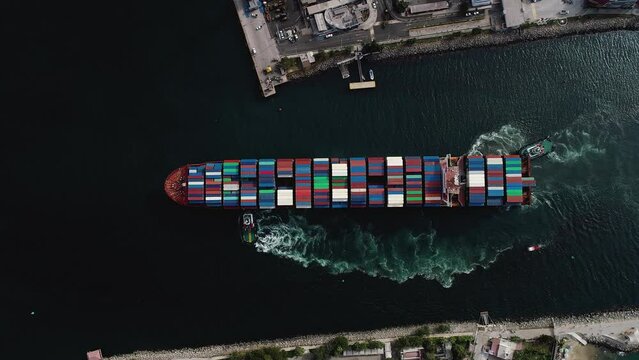 Mega large ULCV container ship fully loaded with crates, sailing away from the harbor - Birds eye, aerial view