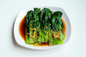 Chinese cabbage with oyster sauce and garlic on a plate on a white background