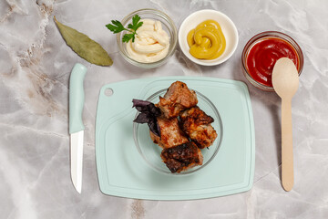 Grilled pork in a glass bowl with fresh basil and sauces.