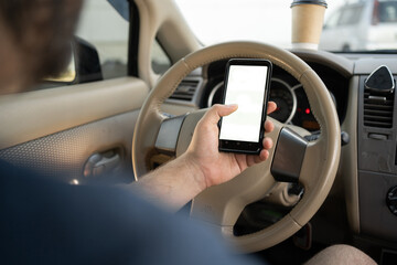 Close-up of male hand holding smartphone with white mockup on screen, background of car steering...