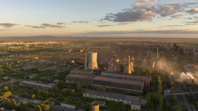 Circling aerial hyperlapse focusing a metal recycling factory emitting vapors at sunset.
