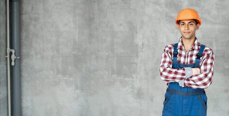 Arabic construction worker portrait in overall and shirt having arms crossed, looking at camera, on the raw concrete wall. Photo of positive young man builder. house renovation, repair