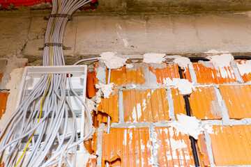 Pile of cables is hanging from a fuse box placed on the wall of unfinished building