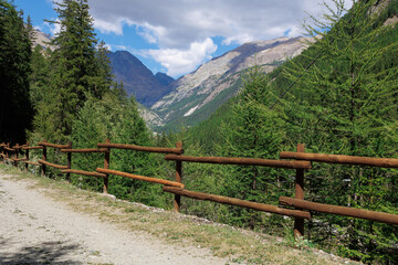 Path with Wooden Fence and in the background Mountain of the Italian Alps and Blue sky with Clouds