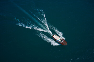 Obraz premium Luxurious wooden motor boat rushes through the waves of the blue Sea. Classic Italian wooden boat fast moving aerial view. Luxurious wooden boat fast movement on dark water.