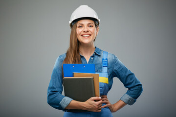 Smiling woman builder in safety helmet and overall holding books and clipboard. Isolated female builder portrait.