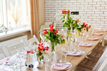 Glasses, forks, knives, napkins and a decorative flower on a dark brown wooden table served for dinner in a cozy restaurant