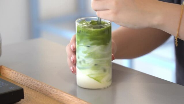 Perfect cup of healthy summer refreshment, young lady placing a straw into the glass and mixing the matcha green tea and the milk evenly and ready to drink.