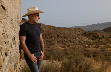 Naklejka premium Portrait of adult man in cowboy hat standing against wall in desert. Almeria, Spain
