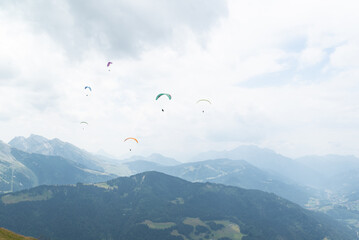 A paraglider group flying over mountain peaks on a cloudy day at french alps. 