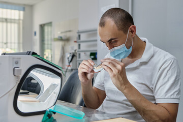 Dentist hand mills tooth crowns created on 3d printer for metal. Dental technician working with ceramic crowns in protective box at the laboratory.