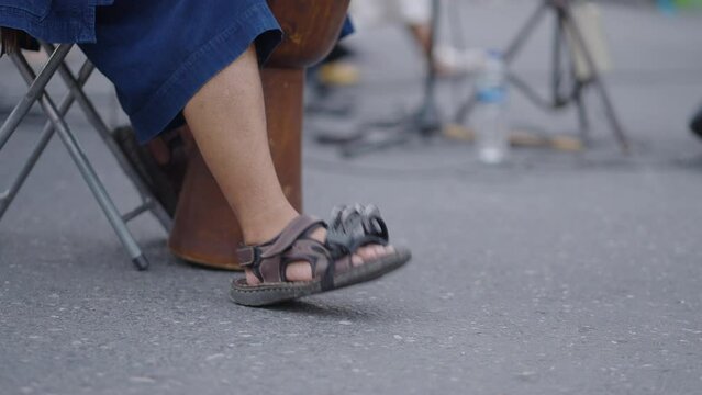 A close up shot of an unidentified man playing Congo in a market. Only his leg is showing which is moving with the beat 