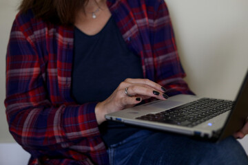 Closeup photo of adult business woman typing on laptop sitting in room. Person put computer on legs and push on touchpad by fingers. Distant work, online communication, modern lifestyle