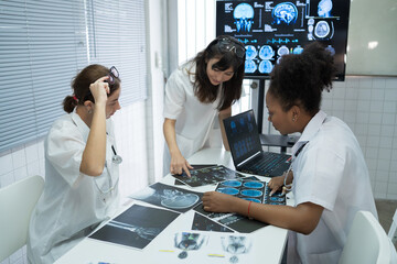 Team of medical doctor meeting in the brain research laboratory by monitor showing MRI, CT scans brain images. Group of female doctor discussing surgery and treatment with medical x-ray scan papers