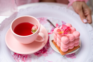 Person hand hold serving festive tray of appetizing creamy cake with butterfly decoration and pink cup of tasty tea with flower petals top view closeup. Pink style decor, holiday, cute service