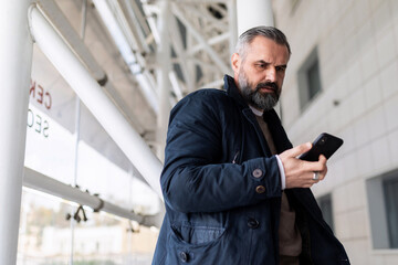 mature man waiting for boarding a flight at the airport looking at his mobile phone