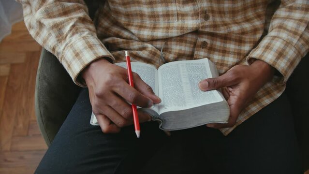 African American man is holding and reading the bible, flipping pages and holding a wooden pencil.