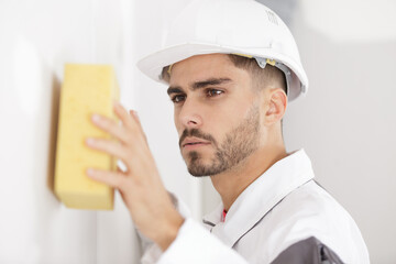 young male builder sponging wall surface