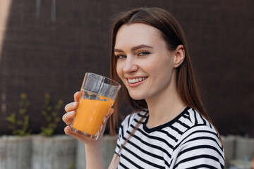 Woman with pretty smile holding in hand glass of refreshing orange drink, portrait closeup....
