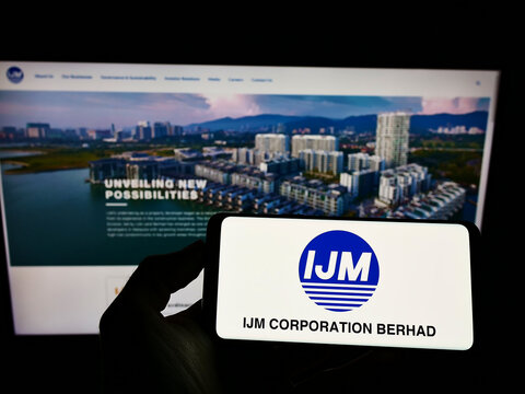 Stuttgart, Germany - 12-12-2021: Person holding mobile phone with logo of Malaysian conglomerate IJM Corporation Berhad on screen in front of web page. Focus on phone display.