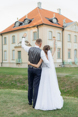 Fototapeta na wymiar Young man groom embracing young wonderful woman bride, raising hands with glasses of wine. Relationship, celebration.