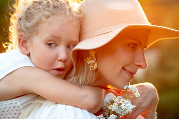 Closeup portrait of mother and little blonde daughter embracing tight from back, walking together...