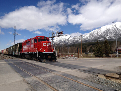 Canmore, Alberta, Canada - May 7 2014 A Canadian Pacific freight train passes a rail crossing. Red locomotive. Canadian Rockies in the background
