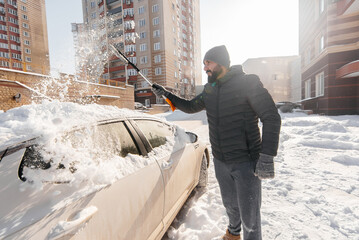 A young man cleans his car after a snowfall on a sunny, frosty day. Cleaning and clearing the car...