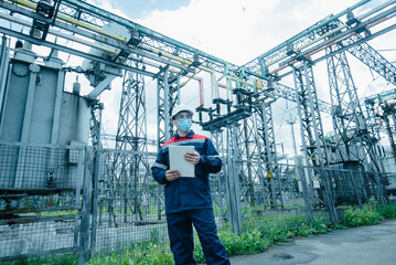 A masked power engineer during a pandemic inspects the modern equipment of an electrical substation before commissioning. Energy and industry. Scheduled repair of electrical equipment.