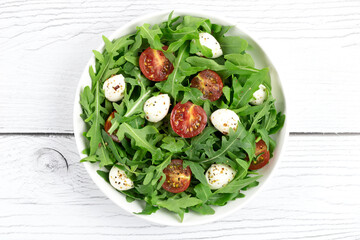 Green salad with arugula, cherry tomatoes and mozzarella cheese on a white wooden background. View from above. 