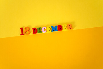 December 18 on a yellow and paper background with wooden and multicolored letters with space for...