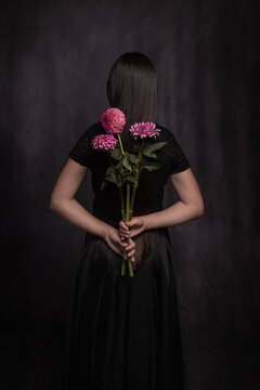 classic studio portrait of woman in black holding pink flowers behind back