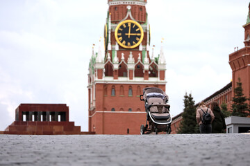 Fototapeta na wymiar Empty baby stroller on Red square in Moscow, view to Kremlin tower and Lenin mausoleum. Concept of demographics and birth rate in Russia