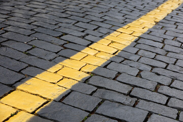 Stone pavement texture, cobbled street. Road marking, yellow line on tiles