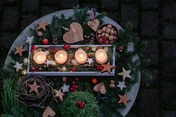 Vier leuchtende Kerzen auf weihnachtlich geschmückten runden Holztisch mit Herzen, Sternen und Tannenzweigen zur Adventszeit