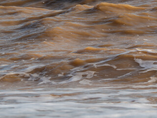 Texture of the water surface with turbid yellow-brown waves close-up