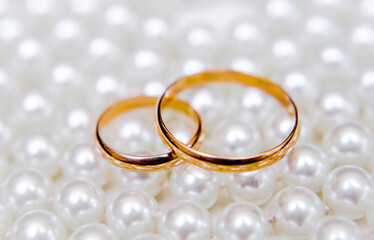 Gold wedding rings lie on a pearl necklace
