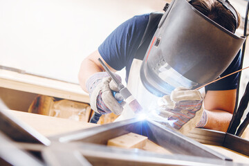 Male in face mask welds with argon-arc welding