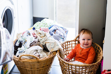 Happy baby sitting in laundry basket helping get wet clothes out of washing machine
