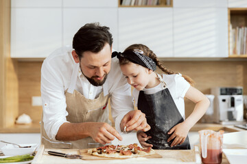 Handsome father with beared taking cheese from homemade pizza tasting. Curious daughter waiting for...