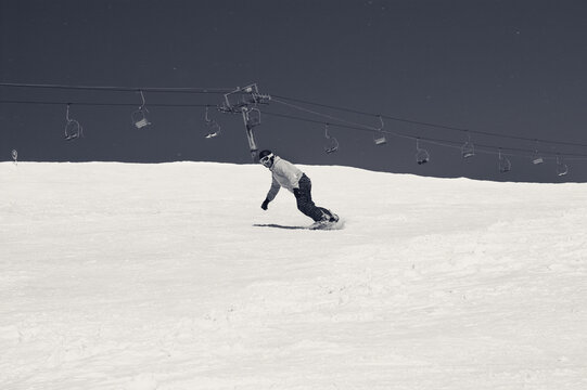 Snowboarder descends on snowy ski slope and sky with snow. Black and white retro toned image.