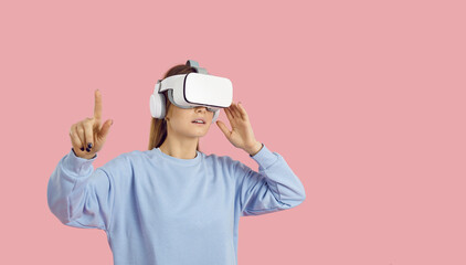 Woman exploring virtual reality. Lady in VR goggles presses, pushes, hits button with finger on touch screen, gets access to videogame level and enters new cyber space, on pastel pink color background