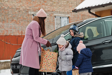 Young woman with children hold eco bags and charging electric car in the yard of her house .